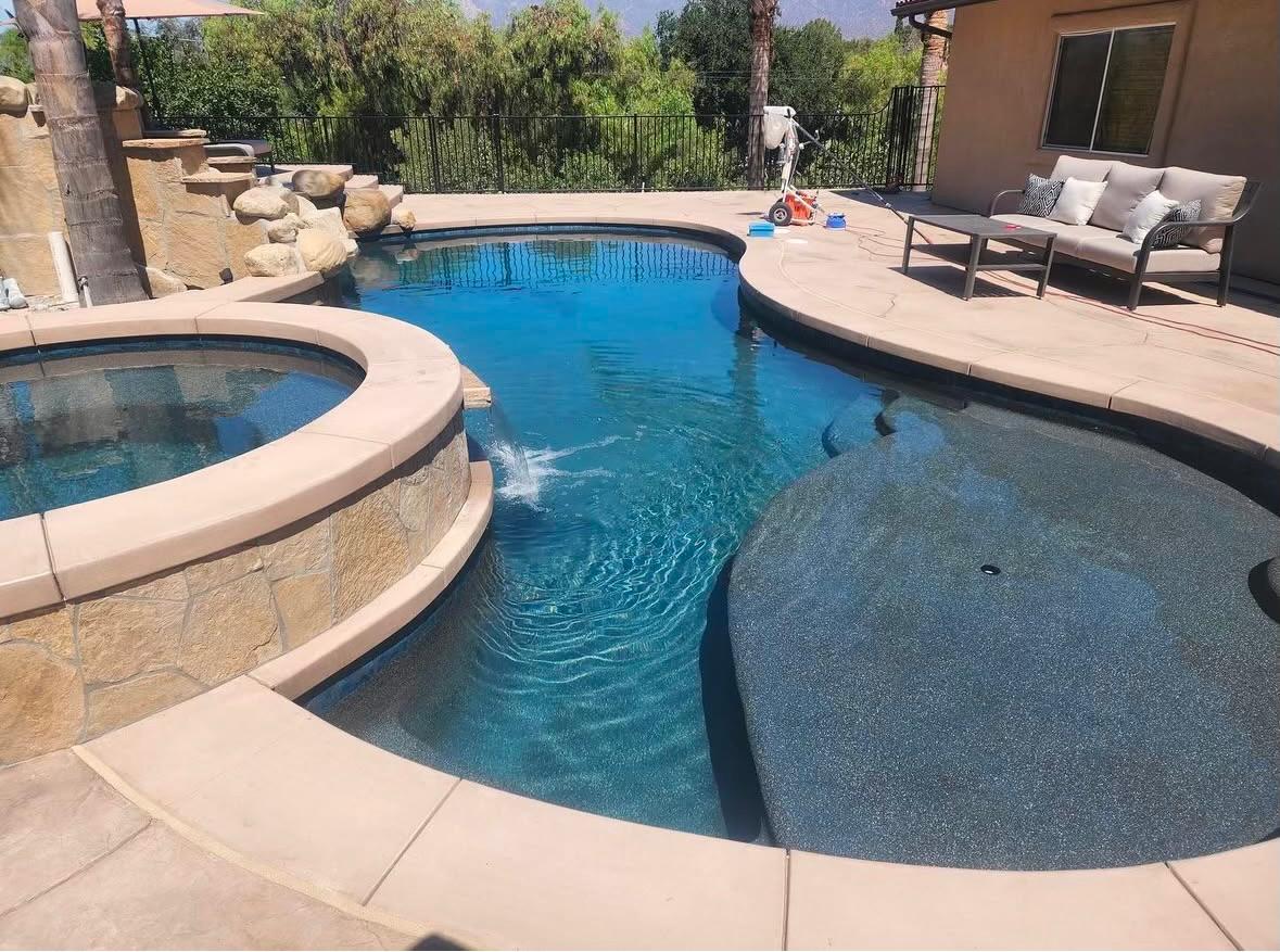 Pool and spa with a spillover feature and a tile-cleaning machine on the deck during a KLUG service call
